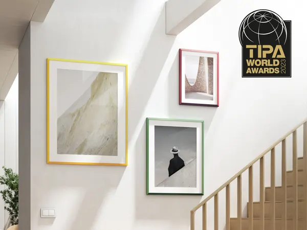 "Best Frame Design" - TIPA 2023 Art gallery wall along staircase with colorful framed photographs and TIPA World Awards logo mounted on white wall