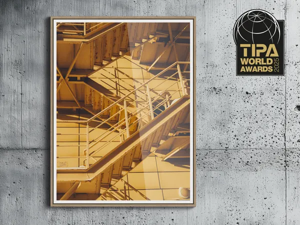 Best Frame Design - WhiteWall Basel 6 mm Industrial staircase in warm golden lighting mounted on concrete wall next to TIPA World Awards logo plaque