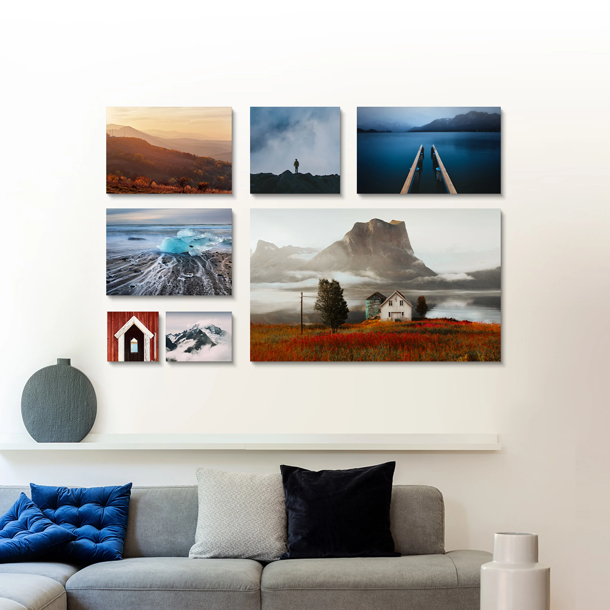 Seven landscape photographs in various sizes on a wall above a gray sofa.
