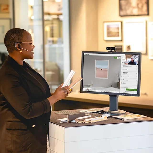 Expert participates in video call at standing desk Woman with headset shows samples in video call in front of computer with product advice.