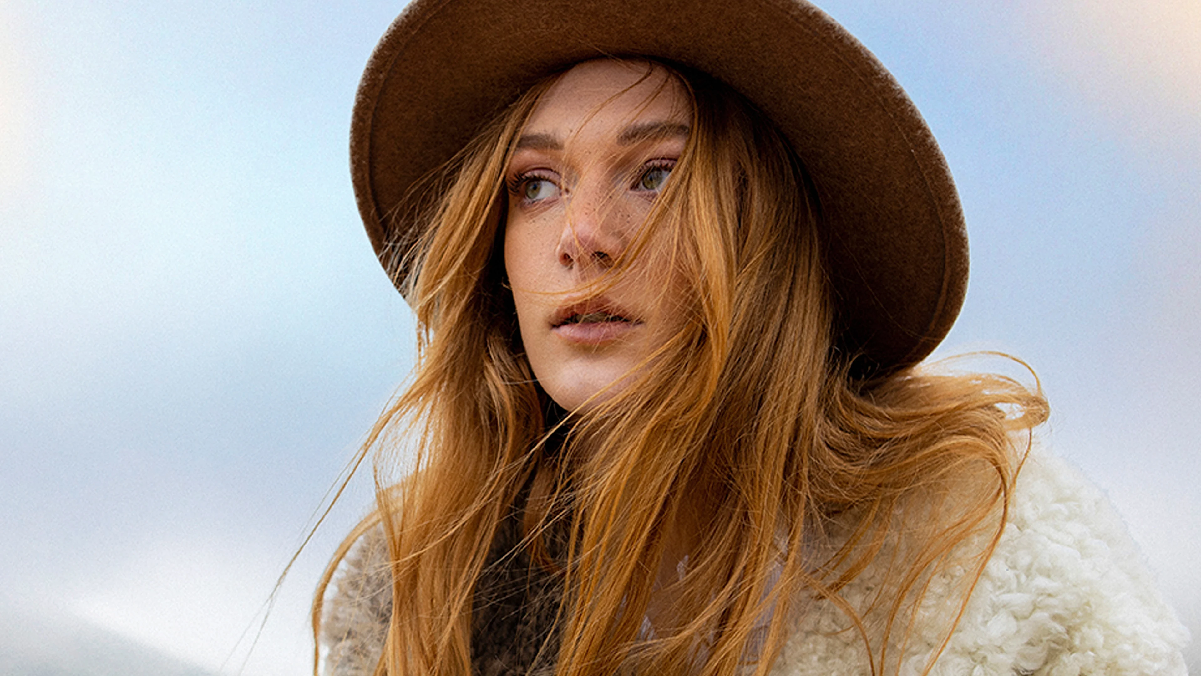 Portrait of women with hat Close-up portrait of person with windswept blonde hair wearing brown wide-brimmed hat and cream sweater against cloudy sky